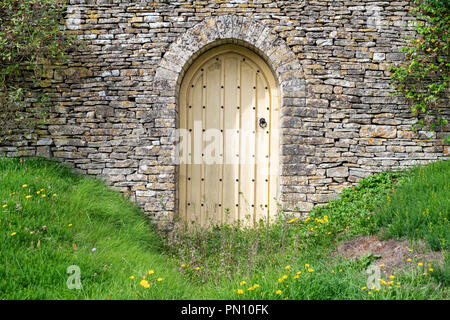 Arcuata giardino in legno porta e cotswold muro di pietra di fronte a una casa nel villaggio Costwold di Calmsden, Cotswolds, Gloucestershire, Inghilterra Foto Stock