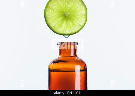 Succo aromatico di calce pezzo gocciolamento in bottiglia di erbe naturali olio essenziale isolato su bianco Foto Stock