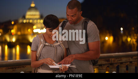 Active africana di un uomo e di una donna ad esplorare Roma sfogliando piccolo libro insieme Foto Stock