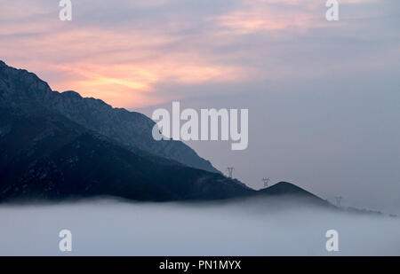 Misty foggy sunrise in montagna con torri di comunicazione a distanza. Foto Stock