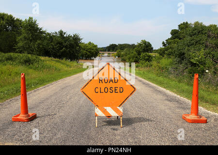 Una strada chiusa segno arancione e costruzione attenzione i coni sono il blocco in un invaso strada rurale sotto un'autostrada cavalcavia. Foto Stock