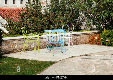 Un tavolo e sedie nel giardino. Acciaio colorato un tavolo e le sedie in piedi in un bellissimo giardino alla giornata di sole. Mobili da giardino. Un set di tre colorati. Foto Stock