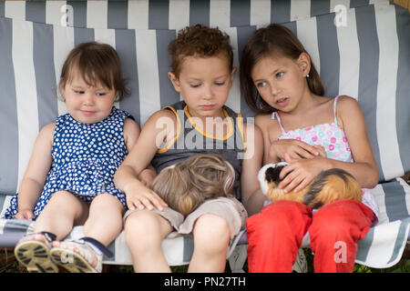 Tre bambini sono seduti in una amaca e suonare la sua cavia animale da compagnia Foto Stock