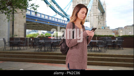 Giovane donna cammina attraverso Londra usando il cellulare per le direzioni Foto Stock