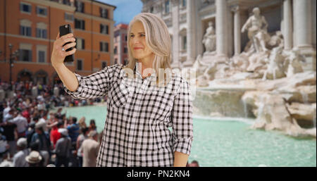 Donna anziana prende un selfie presso la Fontana di Trevi a Roma Foto Stock