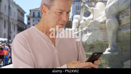 Vecchio maschio caucasico a Roma utilizza smartphone vicino a Fontana dei Quattro Fiumi Foto Stock