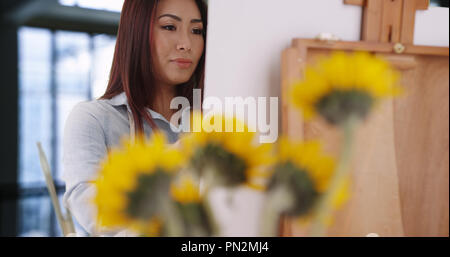 Bella femmina asiatica con calma le vernici girasoli nel suo studio Foto Stock