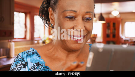 Un anziano americano africano donna usa il suo tablet nella sua cucina Foto Stock