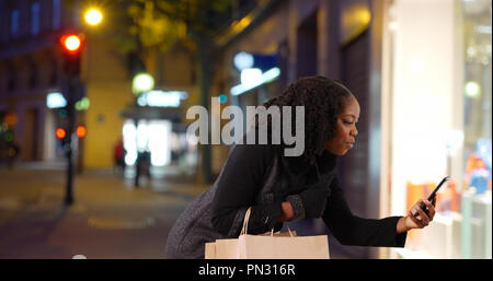 Nero donna si ferma per scattare foto di qualcosa di carino nella finestra di visualizzazione di notte Foto Stock