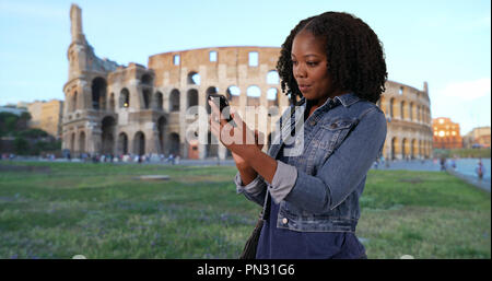 Nero donna in vacanza a Roma la lettura di un messaggio di testo da un amico da Colosseo Foto Stock