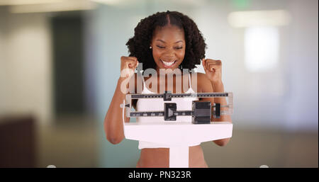 Attraente donna nera che ha perso peso guarda la fotocamera e cheers felicemente Foto Stock