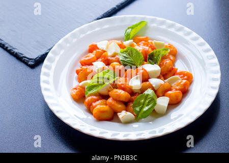 Cotto italiano gnocchi di patate in salsa di pomodoro verde con basilico fresco e mozzarella tagliata a fette sfere servita su una piastra bianca e sfondo nero. Foto Stock