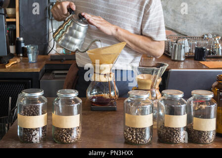 Barista azienda pot antigoccia e versando acqua sulla terra i chicchi di caffè nel filtro di carta per la produzione di birra gocciolare caffè presso la caffetteria al mattino. caffè dri Foto Stock