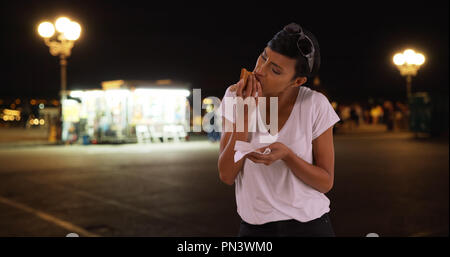 Giovane donna nera gode di fetta di molto cheesy pizza per cena al di fuori Foto Stock