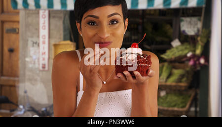 Nero donna mangiare fancy red velvet cupcake con gioia Foto Stock
