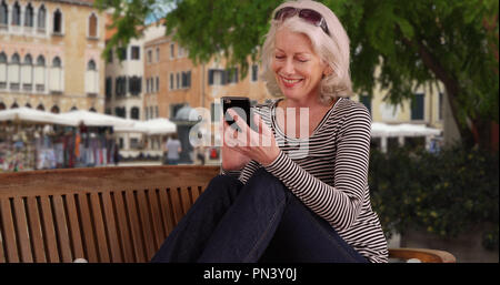 Felice senior donna in vacanza a Venezia gli sms con lo smartphone sul banco di lavoro Foto Stock