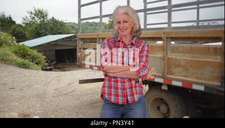 Femmina Senior salariato agricolo in posa con orgoglio nella parte anteriore del carrello in una fattoria impostazione Foto Stock