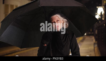 Felice donna più anziana in piedi sotto un ombrellone notte piovosa in città Foto Stock