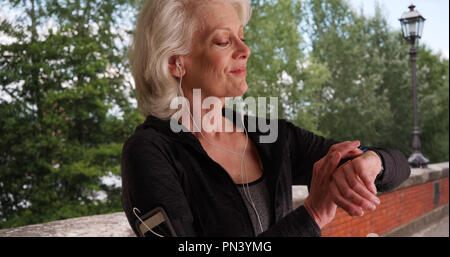Senior donna mettendo in auricolari e verifica il tracker di fitness prima di allenamento Foto Stock