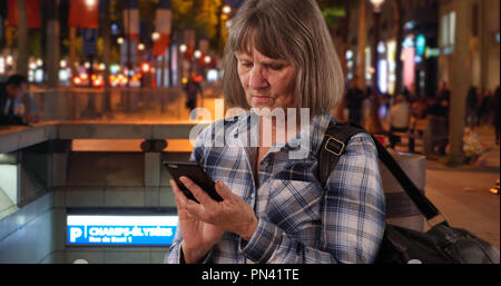 Confuso senior donna utilizza lo smartphone dispositivo per la navigazione su Champs-Elysees Foto Stock