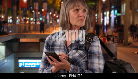 Confuso senior donna utilizza lo smartphone dispositivo per la navigazione su Champs-Elysees Foto Stock