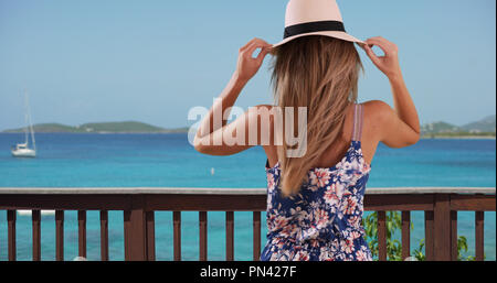 Vista posteriore della donna nella sua 20s tenendo il suo cappello sul patio sul fronte oceano Foto Stock