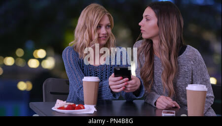 Due cute ragazze tramite telefono cellulare per guardare le foto in esterno e in Parigi Francia Foto Stock