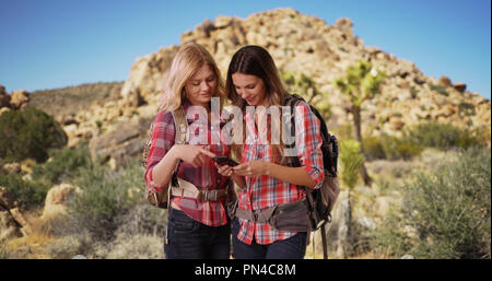 Due attivi femmine caucasica usando il telefono durante un'escursione nel deserto Foto Stock