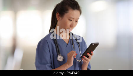 Grave medico millenario in pausa la lettura di testi con lo smartphone all'interno di ospedale Foto Stock