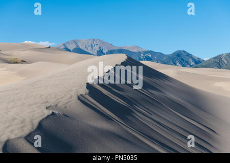 Dune di sabbia e ombre spettacolari e texture di piegarsi verso le montagne rocciose in grandi dune di sabbia del Parco Nazionale, Colorado Foto Stock