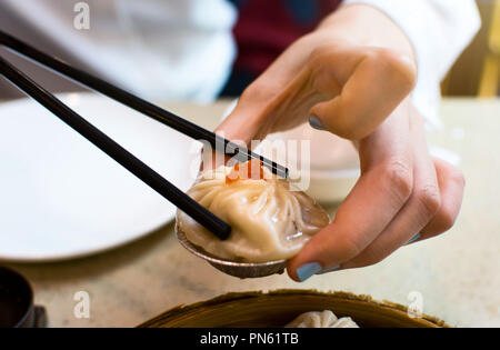 Ragazza prendendo carne di maiale al vapore baozi in zuppa con bacchette Foto Stock