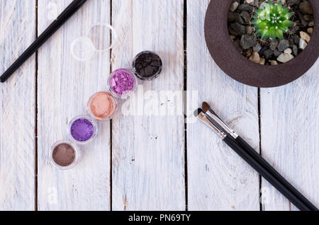 Cosmetici multicolore sul tavolo. Cosmetici, spazzole e vaso di fiori. Giacere piatta. Foto Stock