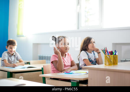 Un gruppo di bambini della scuola di tutti alzando le mani in aria per rispondere Foto Stock