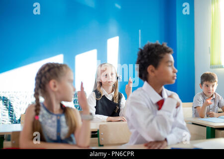 Un gruppo di bambini della scuola di tutti alzando le mani in aria per rispondere Foto Stock