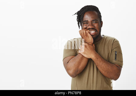 Studio shot di trepida cupo di carnagione scura uomo in abito casual, tenendo la mano vicino alla bocca, mordere le unghie e fissando nervosamente per la rivelazione del segreto in telecamera, sensazione preoccupato in attesa Foto Stock