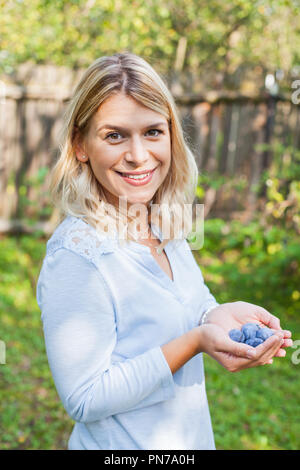 Felice giovane donna nel giardino tenendo un pugno di susine mature Foto Stock