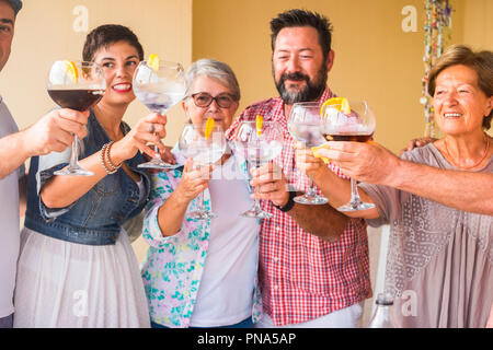 Felice gruppo di età diverse persone che celebra e divertirsi insieme in amicizia a casa o al ristorante. il tifo e tostatura con cocktail e Foto Stock