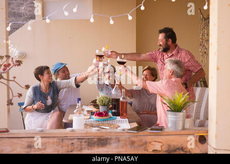 Felice gruppo di età diverse persone che celebra e divertirsi insieme in amicizia a casa o al ristorante. il tifo e tostatura con cocktail e Foto Stock