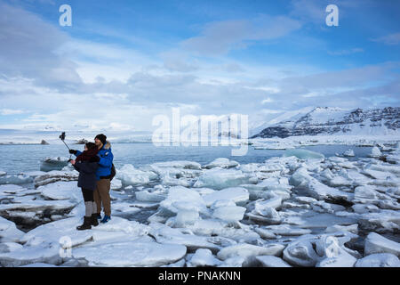 I turisti tenendo selfie fotografia utilizza lo smartphone per le foto delle vacanze a Jokulsarlon laguna glaciale, Vatnajokull National Park, Sud Est Islanda Foto Stock