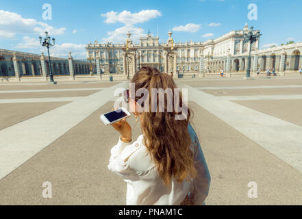 Visto da dietro il viaggiatore moderno donna nella parte anteriore del palazzo reale di ascoltare un audio guida sullo smartphone Foto Stock