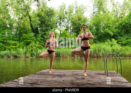 Amici a praticare yoga sul dock dal lago Foto Stock