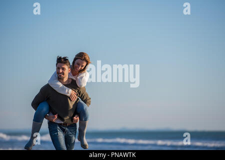 Gli uomini dando Piggy Back corse alla sua ragazza al tramonto sul mare, tempo di autunno Foto Stock