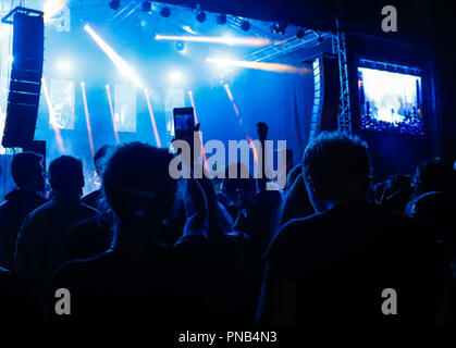 Mano con un telefono cellulare a fuoco il sollevamento dalla folla e prendendo foto nella parte anteriore del palco con luci colorate. Foto Stock