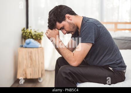 Preoccupato uomo seduto sul letto con la mano sulla fronte in camera da letto in grave stato d'animo le emozioni. Disturbo depressivo maggiore chiamato concetto MDD. Lonely sintomo di m Foto Stock