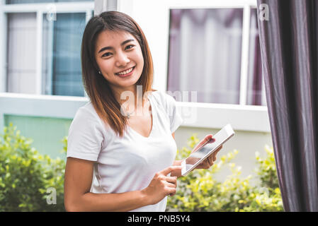 Bellezza donna asiatica ritratto cercando di fotocamera e utilizzando pastiglia per il controllo dell'ordine da parte dei clienti a casa. Business e mezzi di trasporto di consegna concetto. L Foto Stock