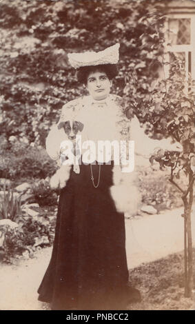 * Vintage fotografia di un elegante Edwardian Lady si fermò nel suo giardino mentre tiene il suo cane Foto Stock