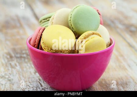 Crunch colorati amaretti in rosa ciotola sul rustico superficie in legno Foto Stock