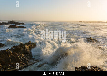 Tempestose onde che si infrangono sulla costa rocciosa al tramonto Foto Stock