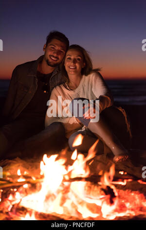 Ritratto di coppia giovane seduto vicino al falò sulla spiaggia di notte di autunno Foto Stock