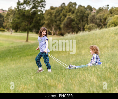 Bambini erba slittino sulla pista da slittino una discesa da una collina in un parco Foto Stock